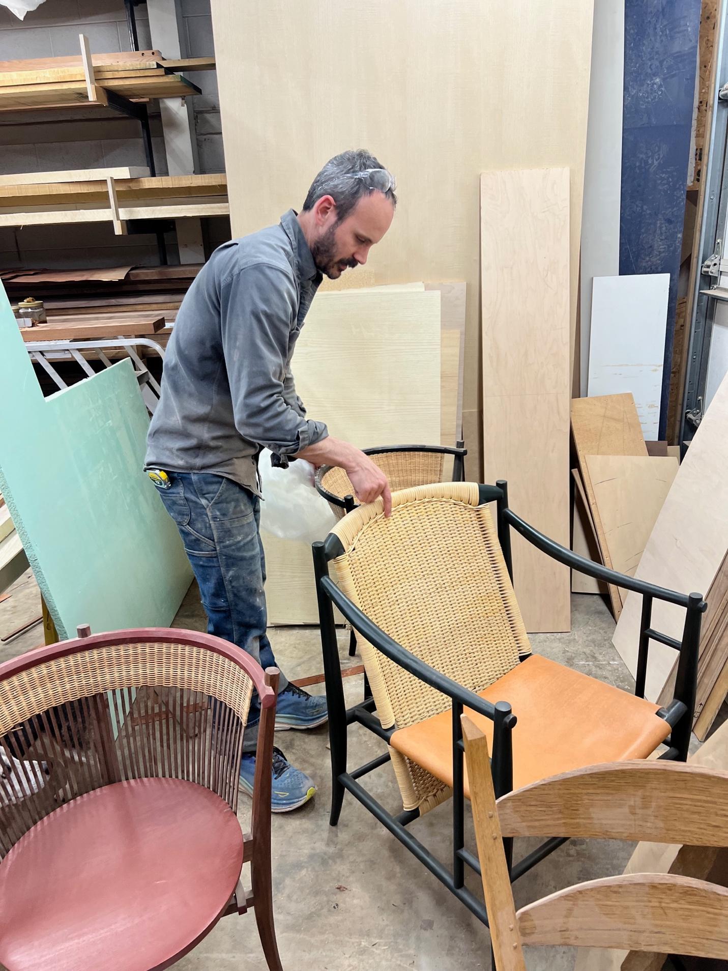 Evan Berding examines the woven seat and frame of a custom chair, blending classical design influences with contemporary form.