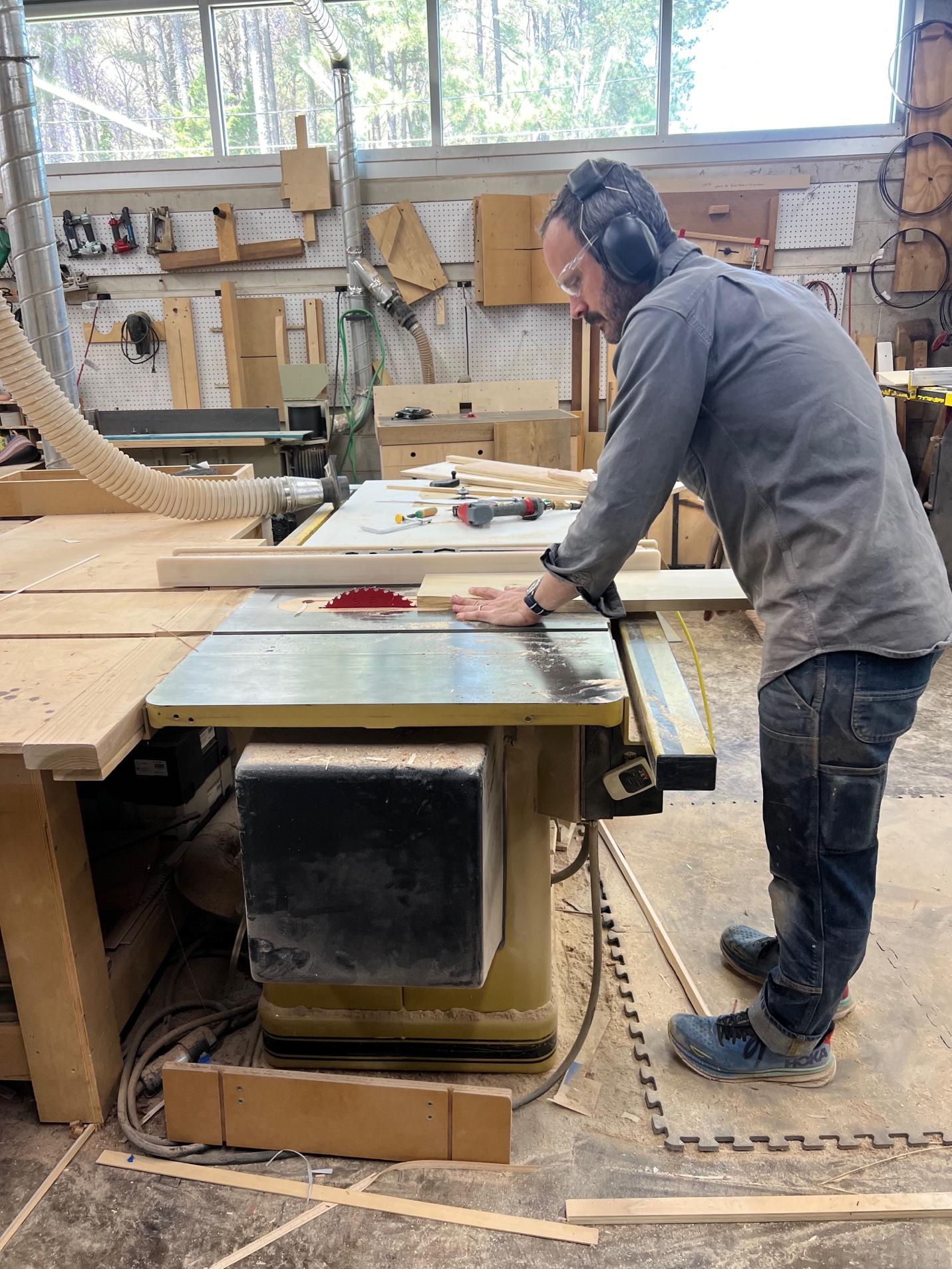 Custom furniture maker Evan Berding uses a table saw in his light-filled Durham workshop while shaping materials for a handcrafted commission.
