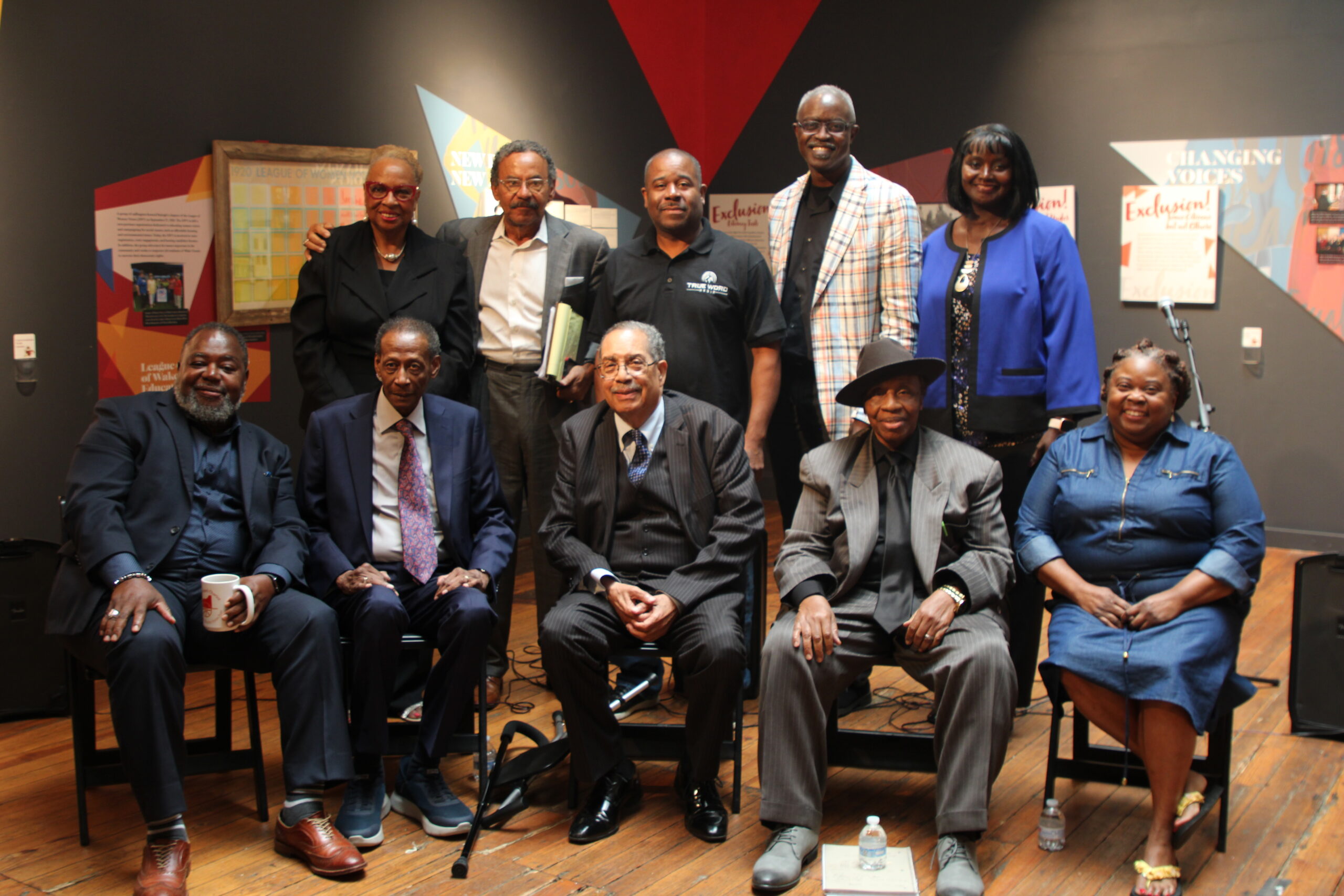 Participants from the Gospel Radio Lab panel discussions pose together on stage, with five people standing in the back row and five seated in the front row.