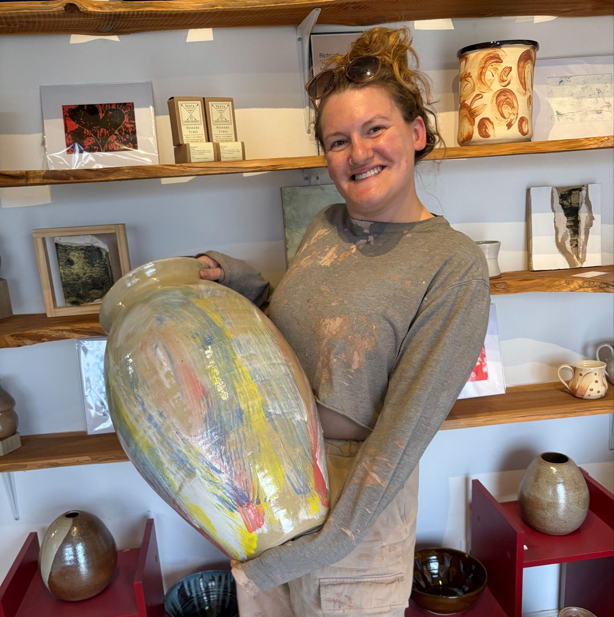 Julie Hinson holding a large finished pottery vessel in her studio.