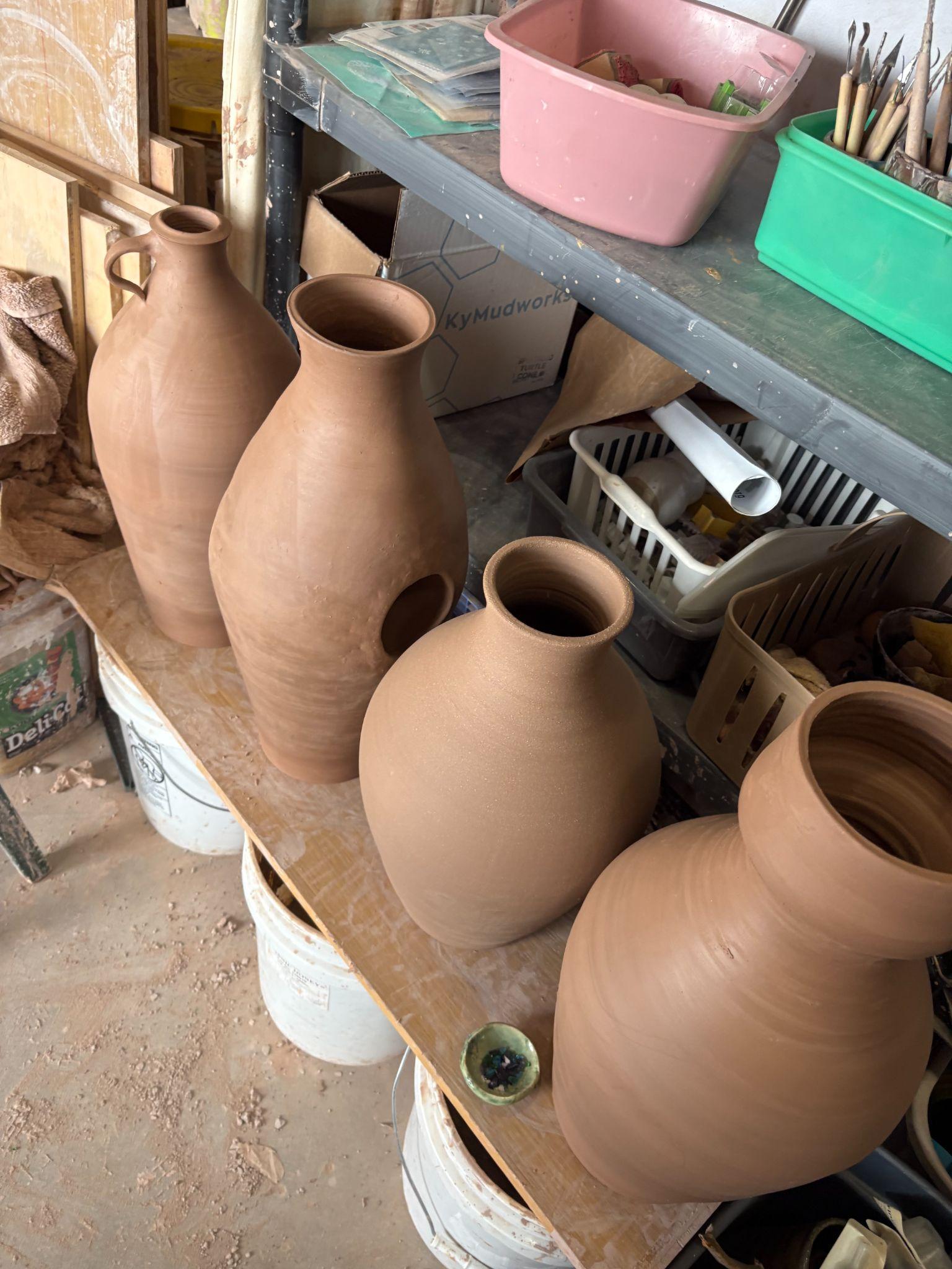 Large clay vessels drying on a shelf in a pottery studio.