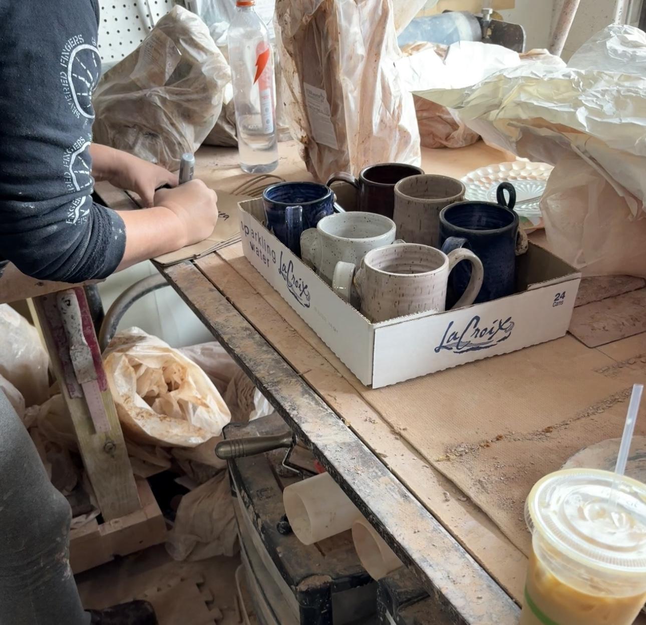 A worktable with clay mugs and pottery materials in Julie Hinson’s studio.