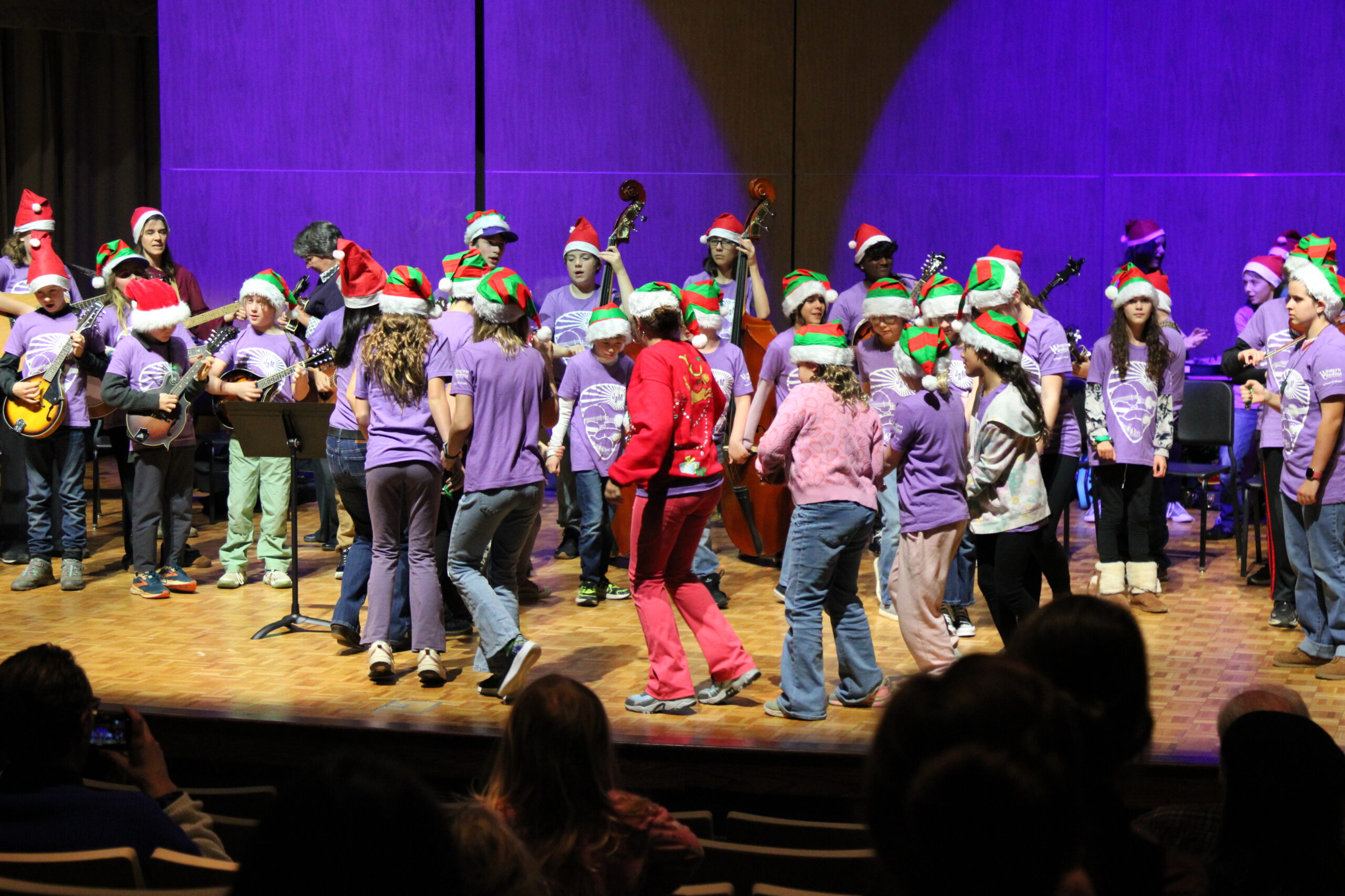 Jackson JAM students perform together on stage during their fall recital, with student musicians standing across the back of the stage and other students dancing in front.