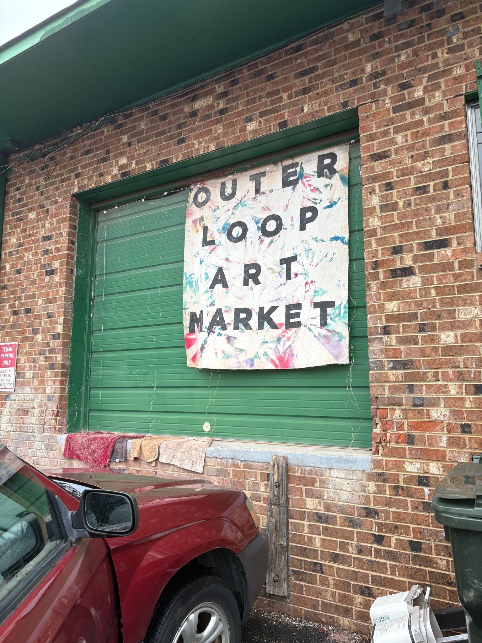 Exterior view of the green garage door with the Outer Loop Art Market sign.